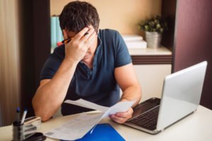 a man sitting at his computer and agonizing over his bills