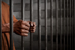 man’s hands holding prison bars